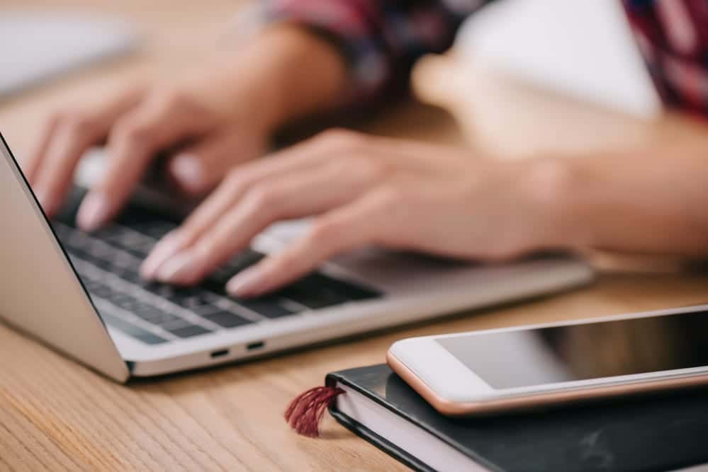 hands typing on laptop, phone sitting beside